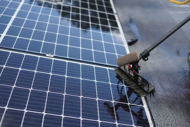 Primer pla d'un raspall de neteja professional passant sobre la superfície humida d'un panell solar.