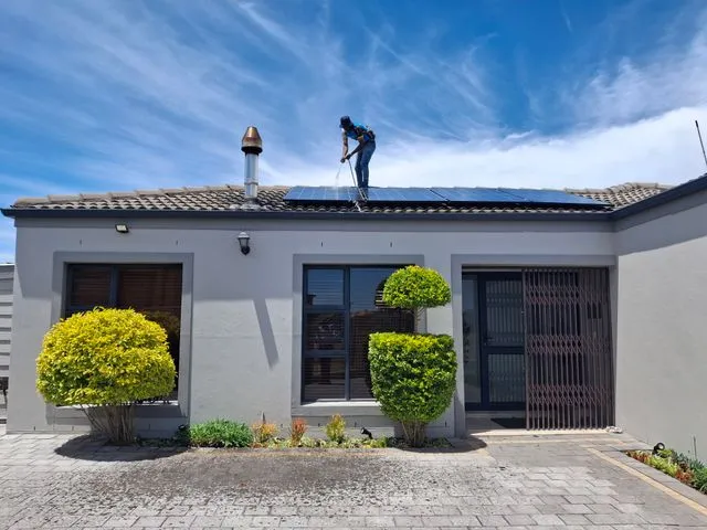 Tècnic professional realitzant tasques de neteja i manteniment amb aigua en una instal·lació solar residencial.