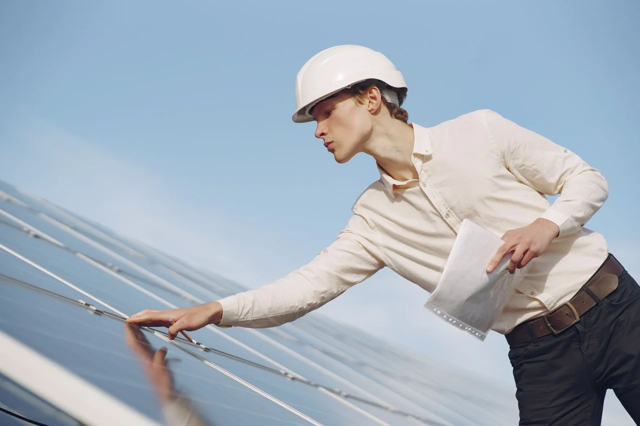 Tècnic de manteniment amb casquet de protecció inspeccionant la superfície d'un panell solar.